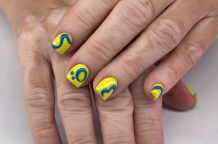 Aplicación de uñas acrílicas cortas en color amarillo vibrante con diseños abstractos en azul en Karla’s Beauty Salon Rincón PR.